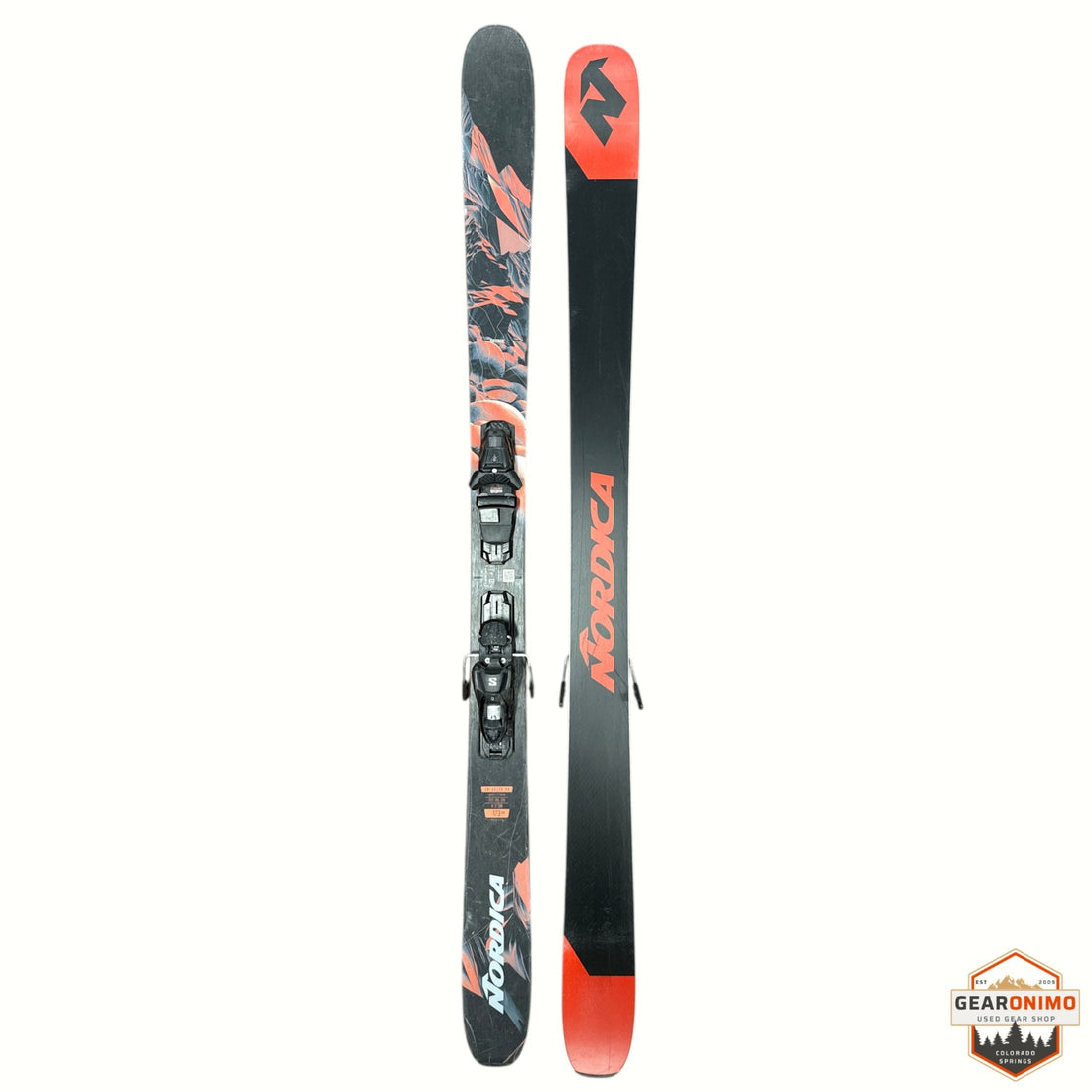 Nordica ski set with bindings, shown vertically against a white background. One ski shows the base with a black, gray, and orange abstract pattern, and the other shows the top with a black shaft, orange 'NORDICA' branding, and an orange tip.