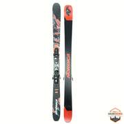 Nordica ski set with bindings, shown vertically against a white background. One ski shows the base with a black, gray, and orange abstract pattern, and the other shows the top with a black shaft, orange 'NORDICA' branding, and an orange tip.