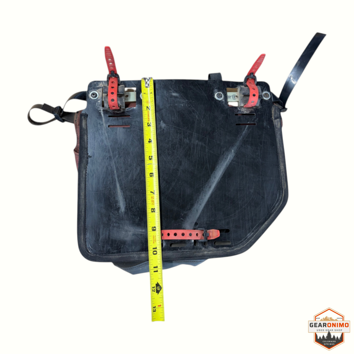 Gearonimo Sports Revelate Designs black bicycle pannier bag with red mounting straps and measuring tape for scale