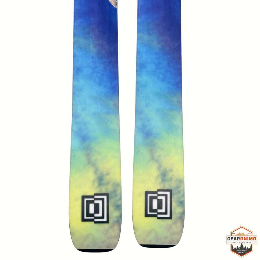Gearonimo Sports K2 Mindbender 99ti skis featuring a blue to yellow gradient tie-dye pattern and square logo graphic