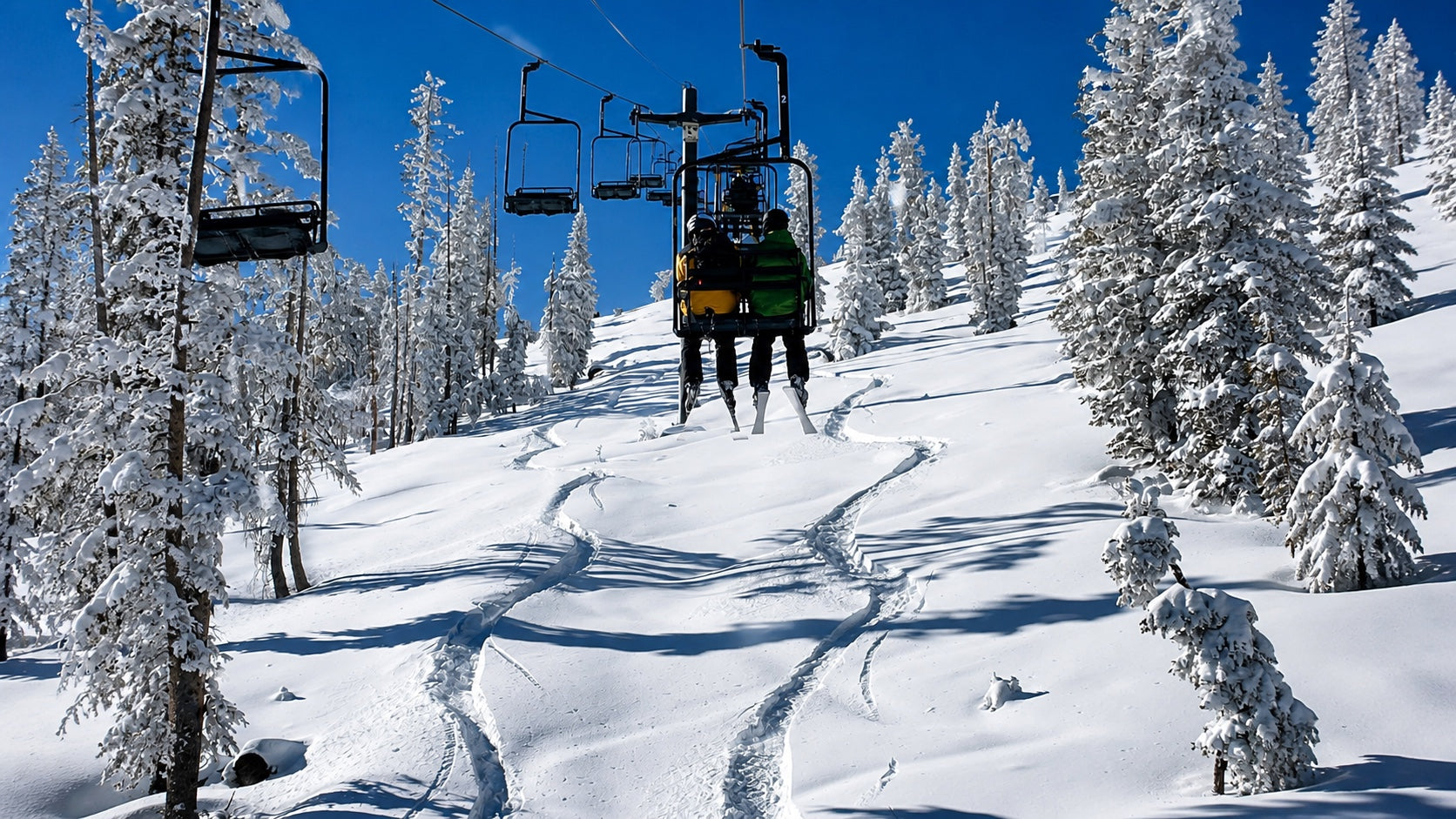 Skiers riding a chairlift over fresh snow and snowy trees